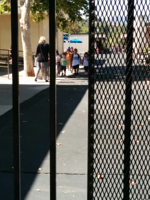 At pick-up time, parents wait outside the gate until students are escorted out by their teacher. The come outside and then line up against the wall by the gate.  You can see little Emrick in green, coming toward the gate with his class. 